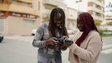 Two african american friends smiling confident using smartphone at street