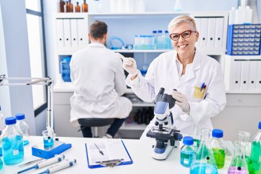 Middle age woman working at scientist laboratory smiling happy pointing with hand and finger to the side 