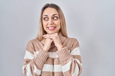 Sarışın bir kadın boğazlı kazak giyiyor. Arka planda mahsur kalmış. Gergin ve heyecanlı bir şekilde gülüyor. 