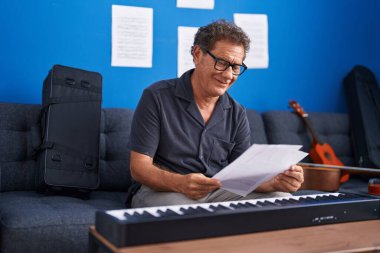 Middle age man musician smiling confident reading music sheet at music studio