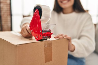 Young hispanic woman smiling confident packing cardboard box at new home