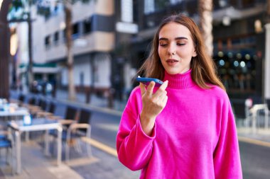 Gülümseyen genç bir kadın caddedeki akıllı telefondan konuşuyor.