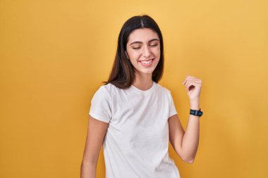 Young beautiful woman standing over yellow background dancing happy and cheerful, smiling moving casual and confident listening to music 
