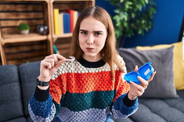 Young hispanic girl holding invisible aligner orthodontic puffing cheeks with funny face. mouth inflated with air, catching air. 