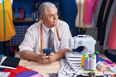 Terzide akıllı telefon kullanan, orta yaşlı, kır saçlı bir terzi.