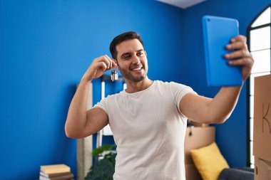 Elinde anahtar olan genç İspanyol adam yeni evinde dokunmatik ped ile selfie çekiyor.