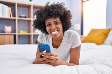 Afrika kökenli Amerikalı bir kadın yatakta akıllı telefon kullanıyor.