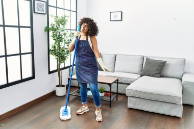 Ortadoğulu genç bir kadın temizlik yapıyor ve şarkı söylüyor. Evde mikrofon olarak paspası kullanıyor.