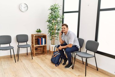 Genç İspanyol adam akıllı telefondan konuşuyor bekleme odasında sandalyede oturuyor.