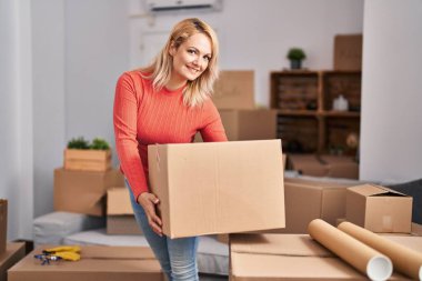 Young blonde woman smiling confident holding package at new home