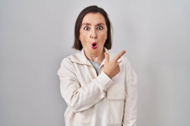 Orta yaşlı, ispanyol bir kadın izole edilmiş arka planda durup parmağını yana uzatarak şaşırmış ve ağzı açık bir şekilde hayret içinde kalmış.. 
