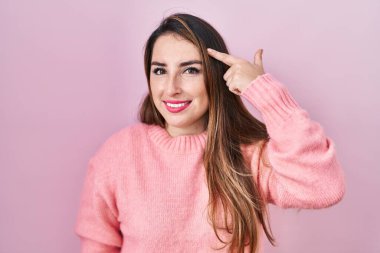 Young hispanic woman standing over pink background smiling pointing to head with one finger, great idea or thought, good memory 