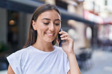 Genç, güzel İspanyol kadın, gülümsüyor. Kafe terasında akıllı telefondan konuşuyor.