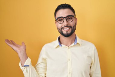 İspanyol genç adam iş kıyafetleri ve gözlük takıyor neşeli bir şekilde gülümsüyor ve avuç içi kameraya bakıyor.. 