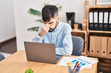 Young hispanic man business worker stressed using laptop working at office
