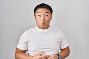Young chinese man standing over white background making fish face with lips, crazy and comical gesture. funny expression. 
