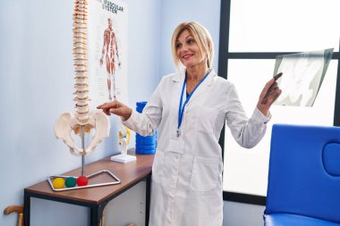 Middle age blonde woman wearing physiotherapist uniform holding xray at physiotherapy clinic