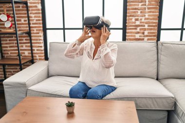 Evde sanal gerçeklik gözlüğü kullanan orta yaşlı bir kadın video oyunu oynuyor.