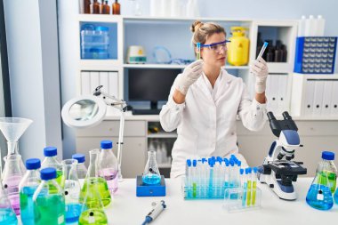 Laboratuvarda test tüpleri tutan bilim adamı üniforması giyen genç sarışın kadın.