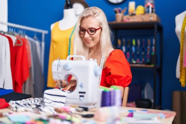 Dikiş atölyesinde dikiş makinesi kullanan kendine güvenen genç sarışın kadın terzi.