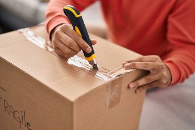 Young hispanic man unpacking cardboard box at new home