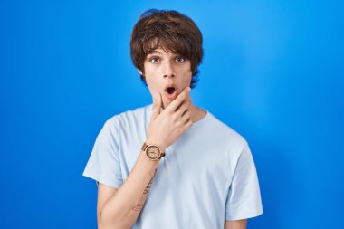 Mavi arka planda dikilen Latin asıllı genç adam elleri çenesinde olan inanılmazlıktan, şaşkınlıktan ve şaşkınlıktan büyülenmiş görünüyor. 