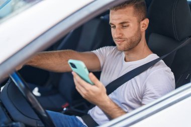 Beyaz bir adam akıllı telefon kullanıyor. Sokakta arabada oturuyor.