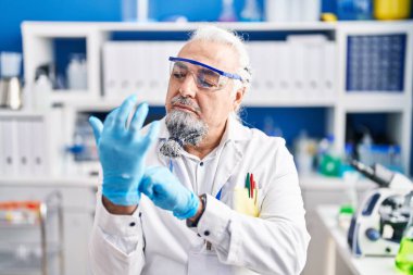 Middle age grey-haired man scientist wearing gloves at laboratory