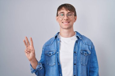 Caucasian blond man standing wearing glasses showing and pointing up with fingers number three while smiling confident and happy. 