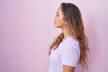 Pembe arka planda duran genç İspanyol kadın yan yan bakıyor, rahat poz veriyor doğal bir yüz ve kendine güvenen bir gülümsemeyle.. 