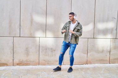 Genç İspanyol adam kendinden emin bir şekilde gülümsüyor müzik dinliyor ve sokakta dans ediyor