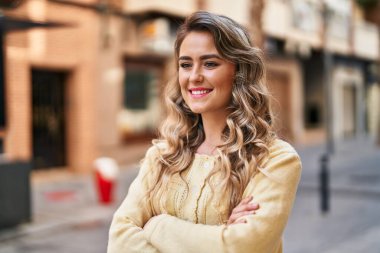 Kendine güvenen genç bir kadın caddede kollarını kavuşturmuş duruyor.