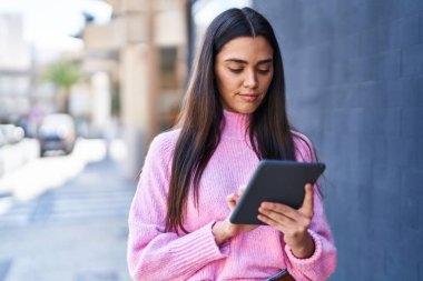 Sokakta dokunmatik ped kullanan genç İspanyol kadın gülümsüyor.