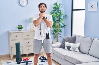 Handsome latin man wearing sportswear at home shouting and suffocate because painful strangle. health problem. asphyxiate and suicide concept. 