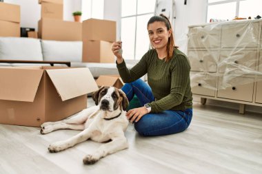 Anahtarı elinde tutan genç bir kadın evde köpekle yerde oturuyor.