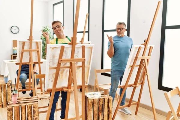 Group of middle age people artist at art studio smiling happy pointing with hand and finger to the side