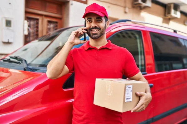 Young Hispanic Man Courier Talking Smartphone Holding Package Street — Zdjęcie stockowe