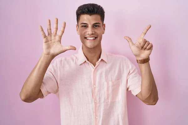 年轻的惊慌失措的男人站在粉红的背景上 用七号手指指指着 面带微笑 自信而快乐 — 图库照片