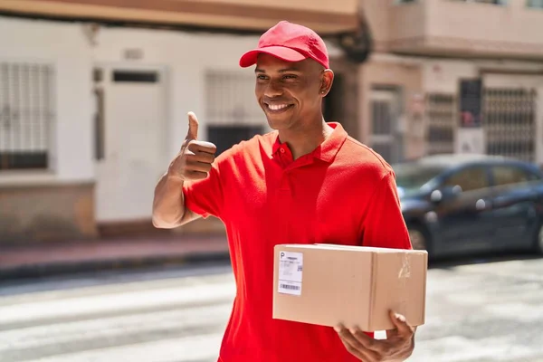 Young latin man delivery worker holding package doig ok gesture with finger at street