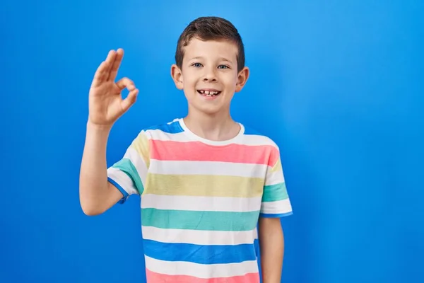Mavi Arka Planda Duran Beyaz Çocuk Gülümsüyor Parmaklarıyla Tamam Işareti — Stok fotoğraf