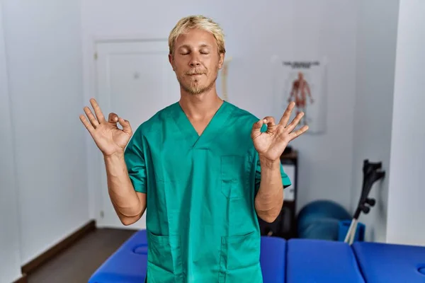 Young Blond Man Wearing Physiotherapist Uniform Standing Clinic Relax Smiling — Stockfoto