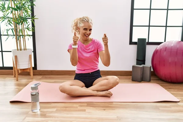 Middle Age Blonde Woman Sitting Yoga Mat Pointing Fingers Camera — Stock Photo, Image