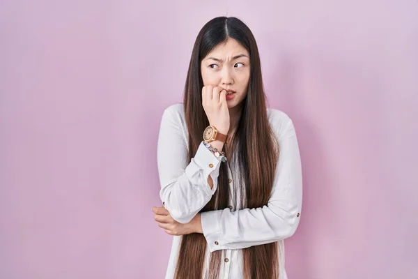 中国年轻女子站在粉红的背景上 双手放在咬指甲的嘴上 显得紧张而紧张 焦虑问题 — 图库照片