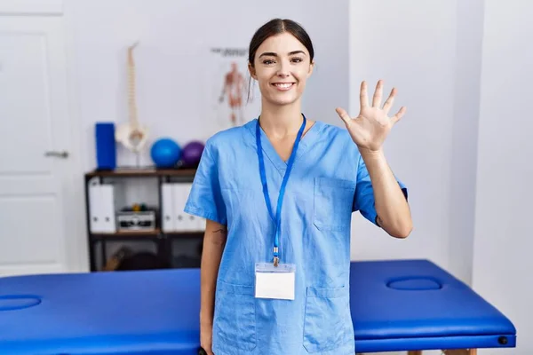 Giovane Donna Ispanica Indossa Uniforme Fisioterapista Piedi Clinica Mostrando Indicando — Foto Stock