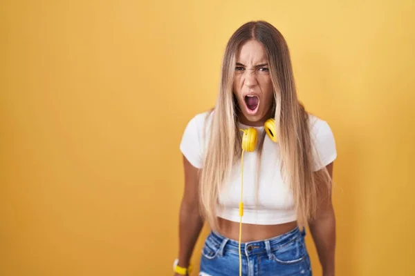 Young Blonde Woman Standing Yellow Background Wearing Headphones Angry Mad — Foto Stock