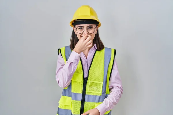 Hispanic Girl Wearing Builder Uniform Hardhat Smelling Something Stinky Disgusting — Zdjęcie stockowe