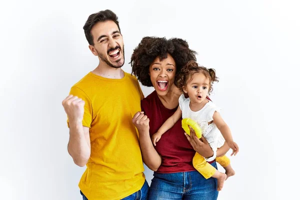 Interracial young family of black mother and hispanic father with daughter very happy and excited doing winner gesture with arms raised, smiling and screaming for success. celebration concept.