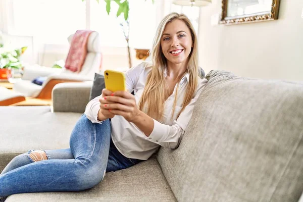Junge Blonde Frau Sitzt Mit Smartphone Hause Auf Dem Sofa — Stockfoto