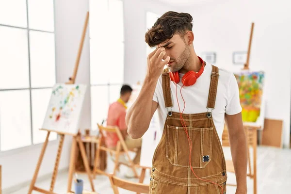 Young hispanic man at art studio tired rubbing nose and eyes feeling fatigue and headache. stress and frustration concept.