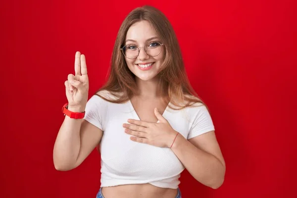 Mladá Běloška Stojí Nad Červeným Pozadím Usmívá Rukama Prsou Prsty — Stock fotografie